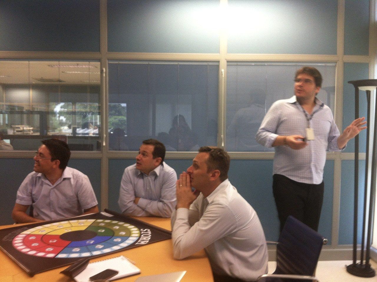 Fernando Palacios conduzindo uma sessão de storytelling com uma equipe corporativa sentada ao redor de uma mesa de reunião